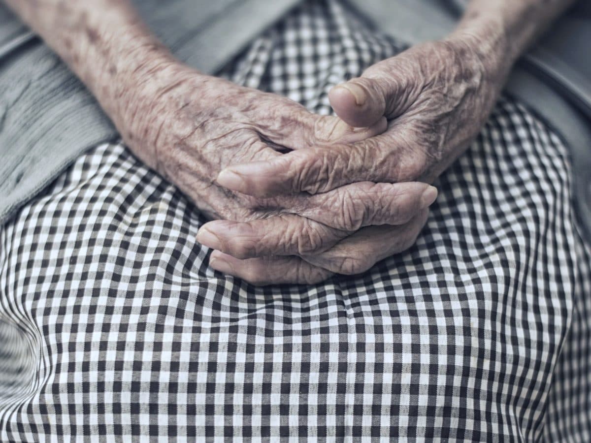 Les mains posées d’une personne âgée assise, photographiées de près.